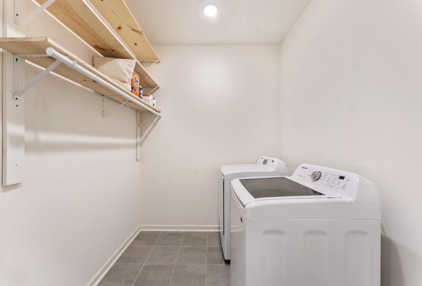 Dedicated laundry area featuring a tiled floor, white baseboards, and built-in wood shelving with a hanging rod