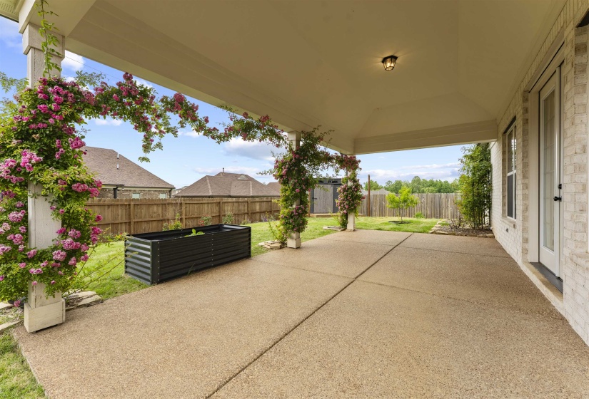Spacious covered patio featuring an exposed aggregate concrete surface, white brick exterior, and a privacy fence