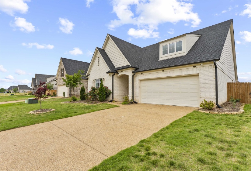 Contemporary home with a white brick and siding facade, featuring a two-car garage, dormer window, dark shingle roof, and a concrete driveway
