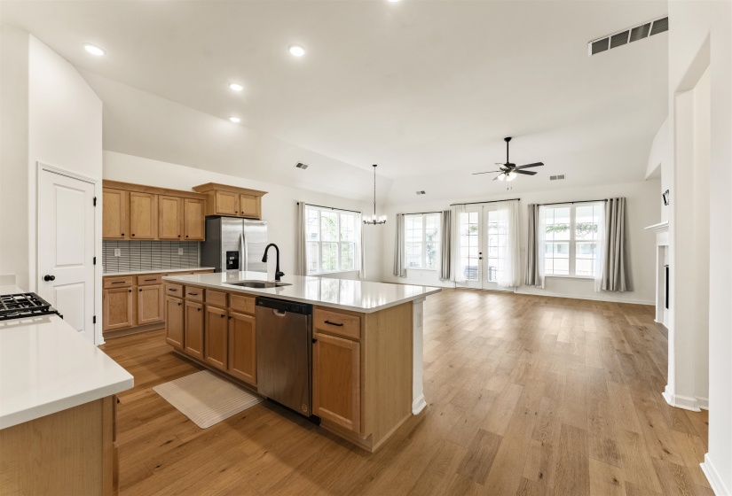 Open-concept interior featuring wood-finish flooring, vaulted ceilings, a kitchen island with sink, and double glass panel doors