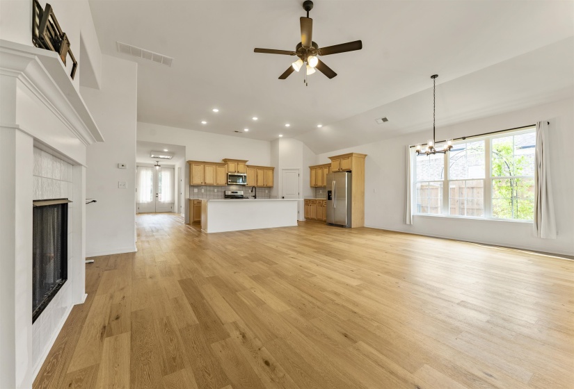 Spacious living area featuring wood-finish flooring, a white fireplace with tile surround, vaulted ceilings, and recessed lighting