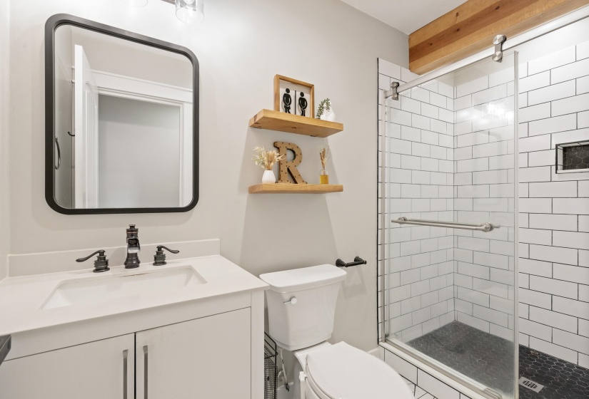 Glass-enclosed shower with white subway tile surround and dark hexagonal tile flooring