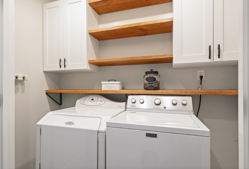 Dedicated laundry space featuring white cabinetry with black hardware, natural wood-finish shelving, and a natural wood-finish countertop