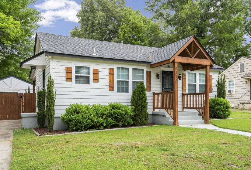 White siding exterior with a prominent gabled front porch featuring dark wood architectural details and railing