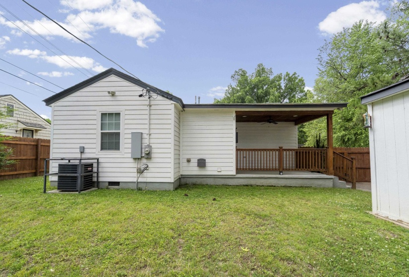 Expansive backyard featuring a covered patio with wood railing and ceiling fan, white siding exterior, and a detached storage shed