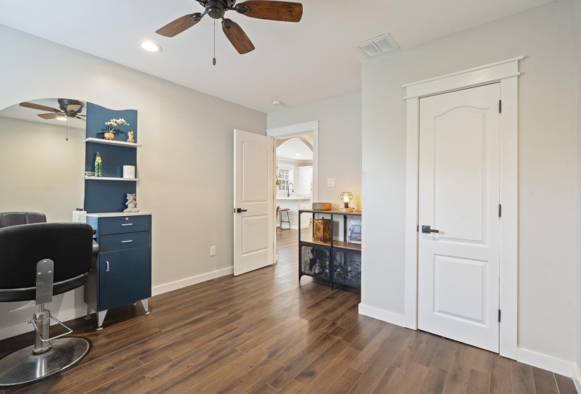 Interior room featuring wood-finish flooring, a ceiling fan with integrated lighting, and multiple panel doors with dark hardware