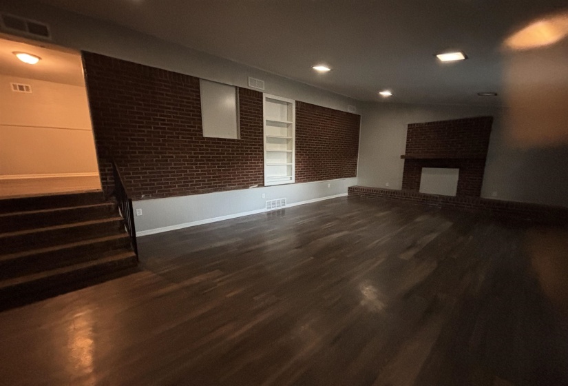 Spacious living area featuring wood-finish flooring, recessed lighting, and a brick accent wall with built-in shelving
