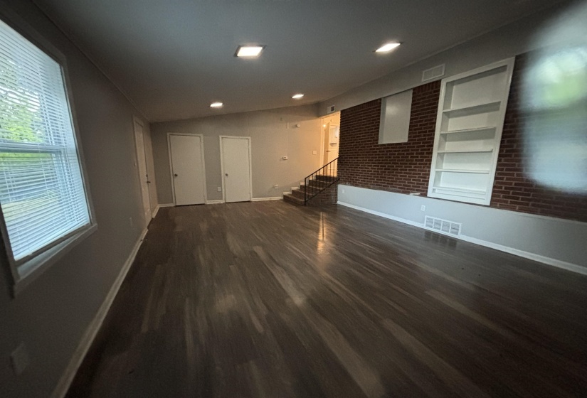 Spacious room featuring wood-finish flooring, a prominent exposed brick wall, and built-in shelving