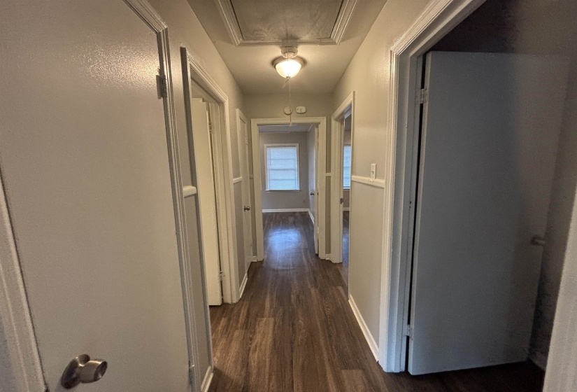 Hallway featuring wood-finish flooring, light grey painted walls, white trim, and multiple doorways