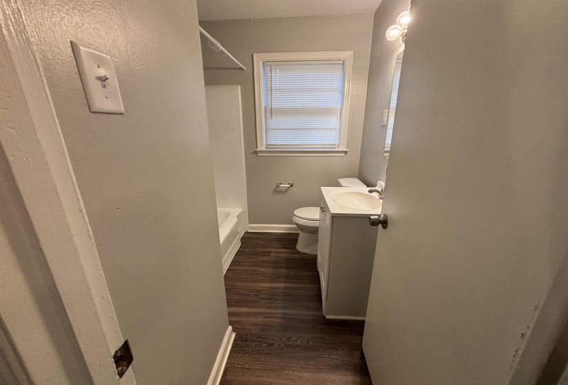 Bathroom featuring a white vanity with an integrated sink, wall-mounted light fixture, and wood-finish flooring