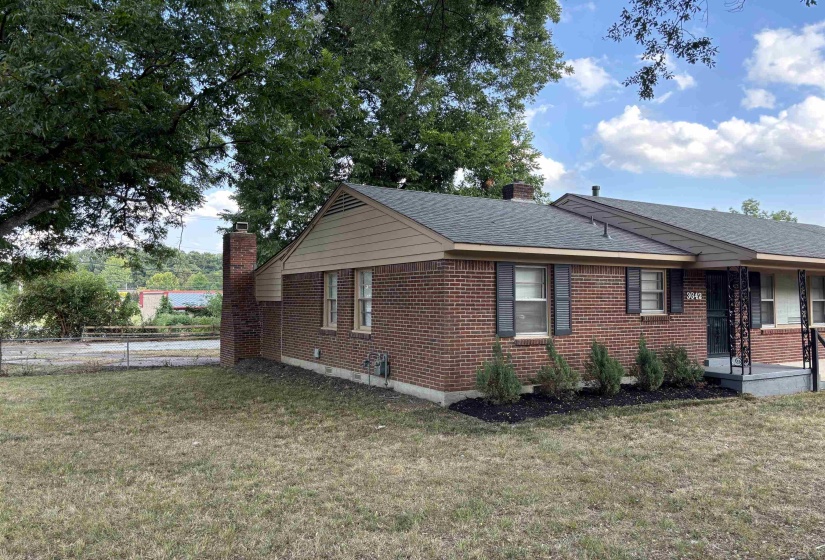 Brick exterior with dark shutters, a front porch featuring black metal railings, and a side chimney