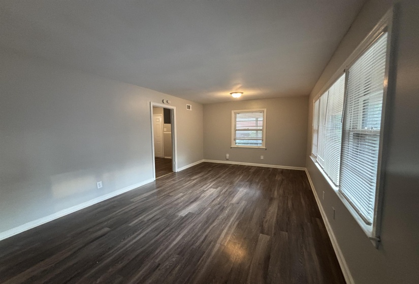 Spacious room featuring wood-finish flooring, light gray walls, white baseboards, and multiple windows with horizontal blinds