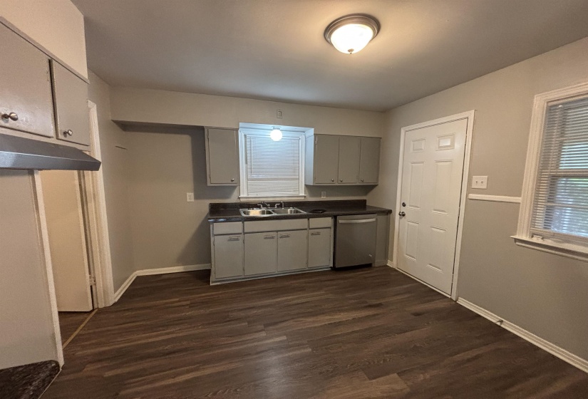 Kitchen featuring wood-finish flooring, gray cabinetry, dark countertops, a stainless steel dishwasher, and a double-basin sink