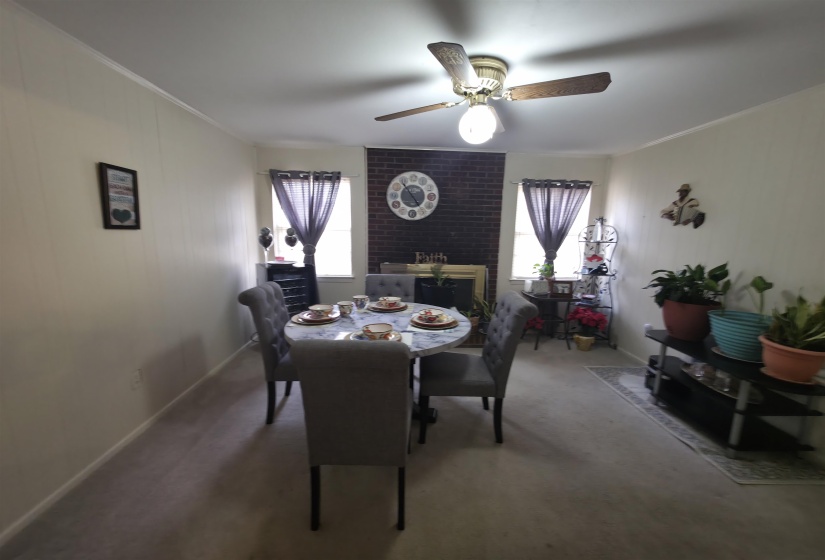 Living space featuring a brick-clad fireplace, ceiling fan with integrated lighting, and neutral wall paneling