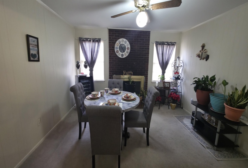 Dining area featuring a brick accent wall with a decorative mantel, carpeted flooring, and a ceiling fan with light fixture