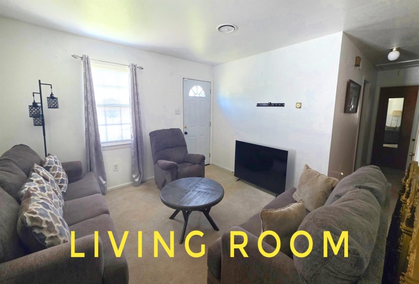 Carpeted living area featuring white walls and a window with white trim
