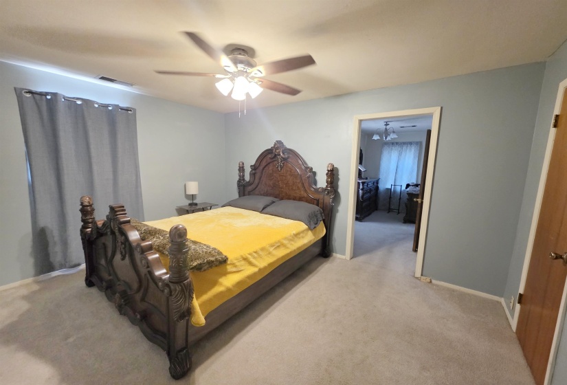 Spacious room featuring light blue walls, soft gray carpeting, a ceiling fan with integrated lighting, and a doorway opening to another room