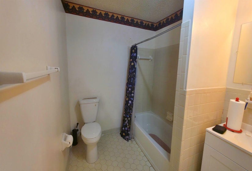 Bathroom featuring a white toilet, white bathtub with shower, vanity with a countertop, and hexagonal floor tiling