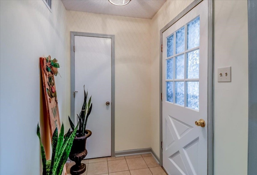 Entryway featuring a six-pane glass panel door with gold-tone hardware, a solid white door, light-colored wall paint, and neutral tile flooring