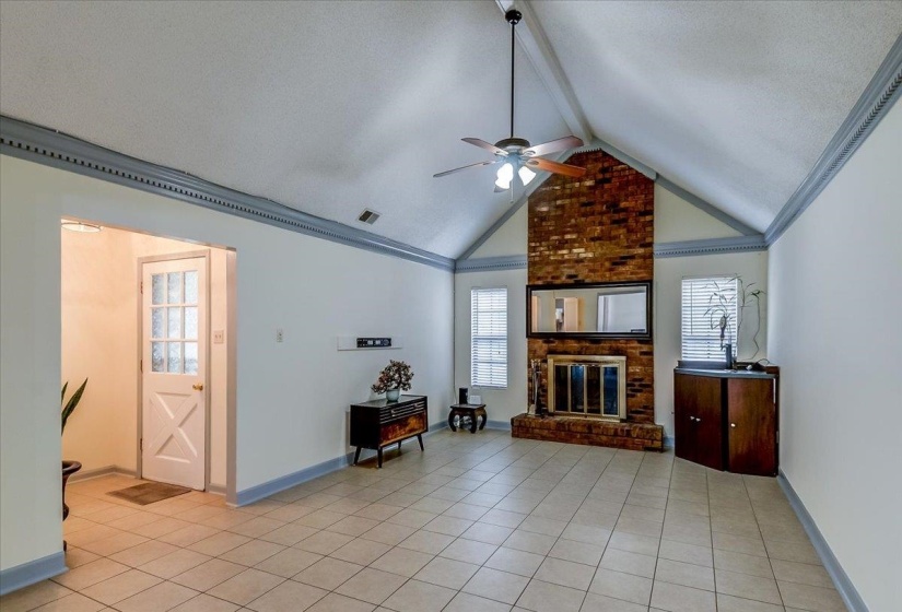 Spacious living area featuring a vaulted ceiling with a ceiling fan, a brick fireplace, and tile flooring