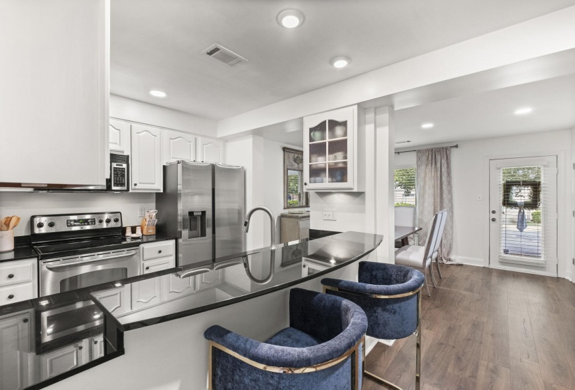 Kitchen featuring black countertops with an integrated breakfast bar, white cabinetry, stainless steel appliances, and wood-finish flooring