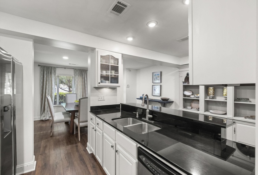 Kitchen featuring black countertops, a stainless steel double-basin sink with a pull-down faucet, white cabinetry with dark hardware, and wood-finish flooring