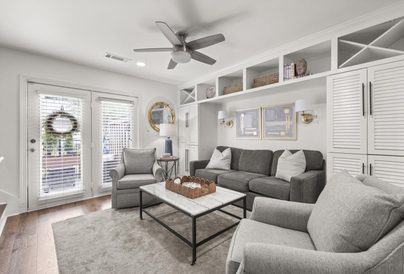 Living area featuring built-in shelving, white louvered cabinetry, and a ceiling fan