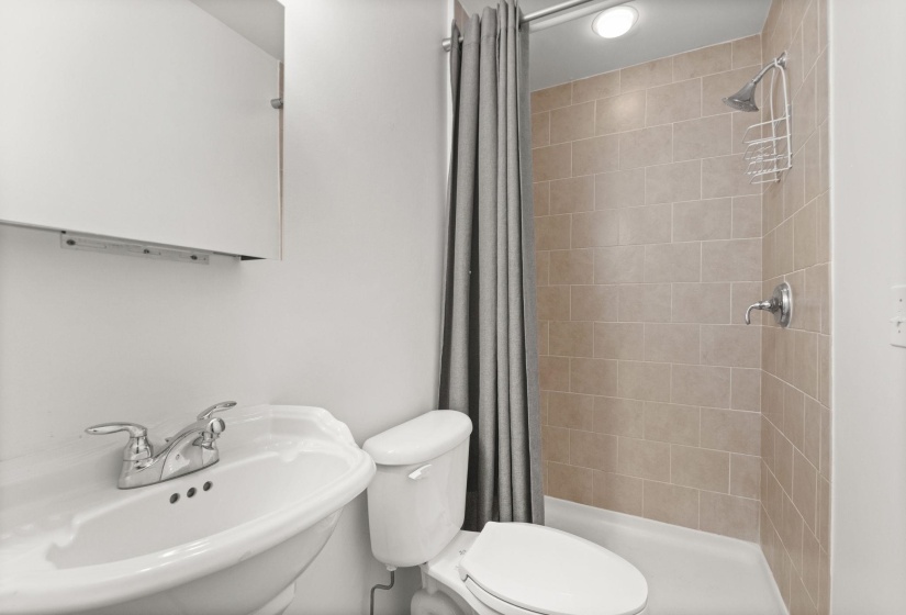 Bathroom featuring a pedestal sink, white cabinetry, a toilet, and a tiled shower with a white pan and chrome fixtures