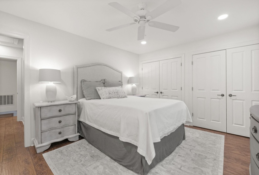 Bedroom featuring wood-finish flooring, white walls, and multiple built-in closet doors with dark hardware
