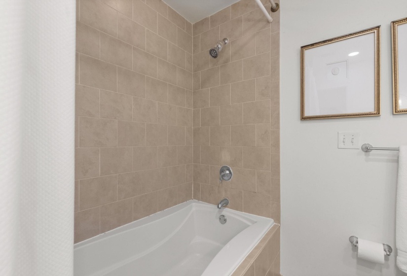 Bathtub and shower combination featuring neutral-toned tile surround, chrome fixtures, and a white tub