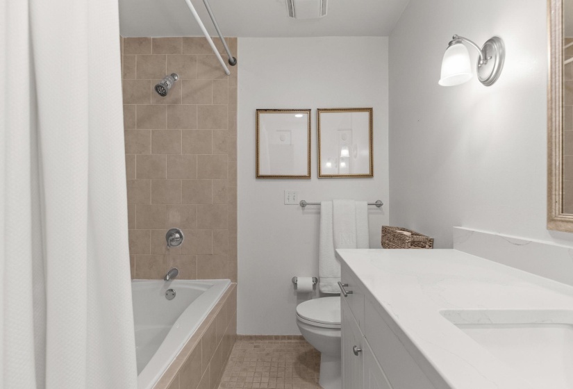 Bathroom featuring a white bathtub with tile surround, a built-in vanity with a white countertop and undermount sink, and a sconce light fixture