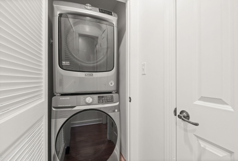 Stackable washer and dryer unit within a dedicated closet space, featuring louvered bifold doors and dark wood-finish flooring