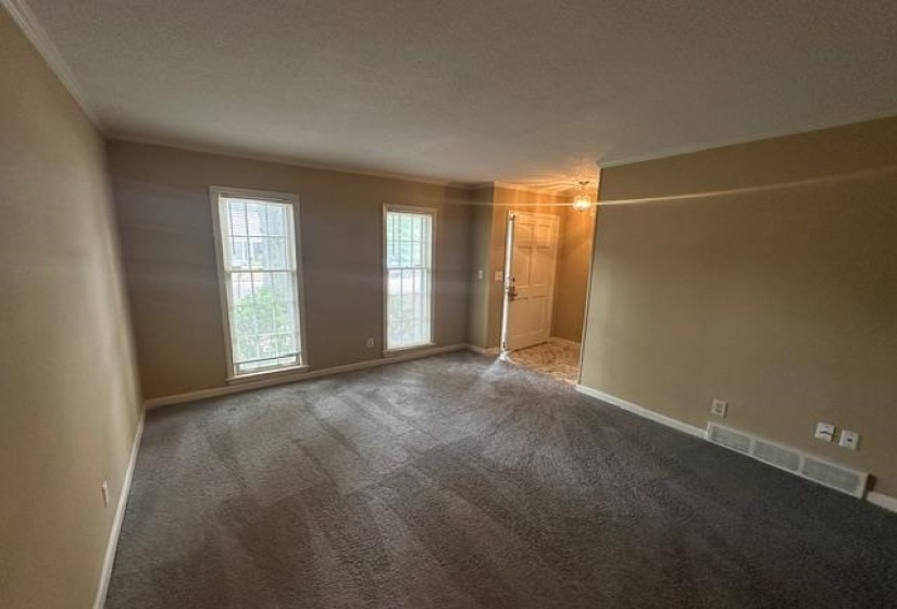 Spacious room featuring neutral carpeting, two double-hung windows, and a white entry door with a decorative glass light fixture