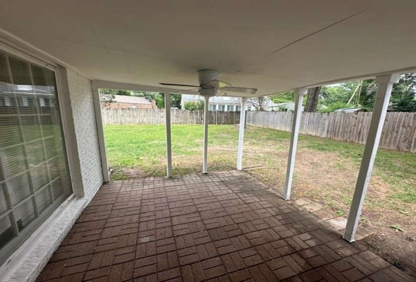 Covered patio featuring a brick-patterned floor, ceiling fan, and white painted brick exterior