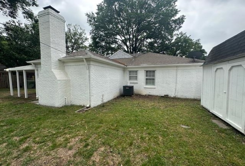 Rear exterior featuring a painted brick finish, a prominent chimney, a covered patio with white columns, a detached storage shed, and a visible HVAC unit