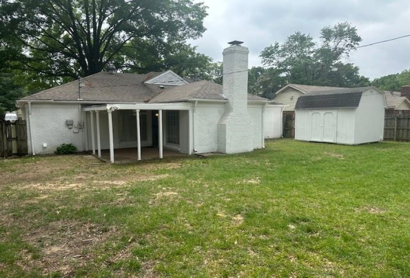 Expansive backyard featuring a covered patio, brick chimney, and a storage shed