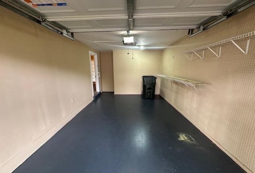 Single-car garage featuring a roll-up door, painted concrete flooring, an interior access door, pegboard wall, and built-in shelving