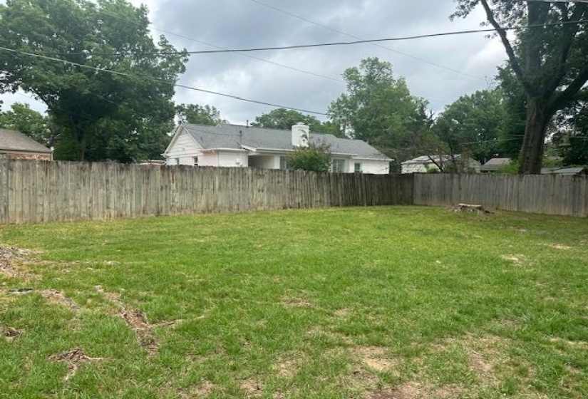 Spacious backyard featuring a wooden privacy fence, expansive green lawn, and mature perimeter trees