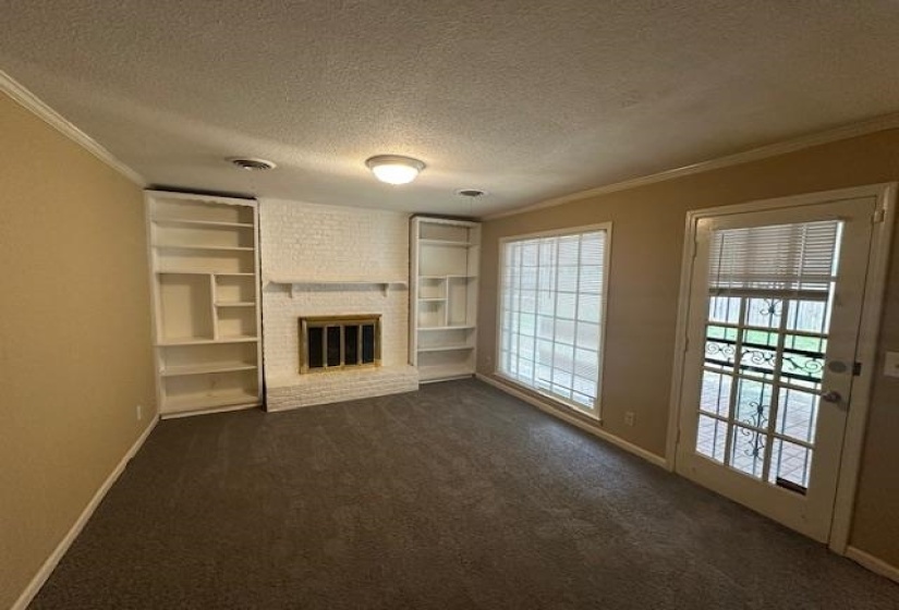 Living area featuring a white brick fireplace with a brass firebox, flanked by built-in white shelving units