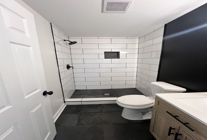 Bathroom with a shower stall, vanity, and dark tile patterned flooring