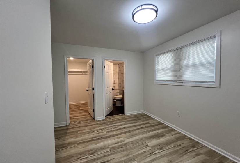 Unfurnished bedroom featuring a walk in closet, light wood-style flooring, and ensuite bath