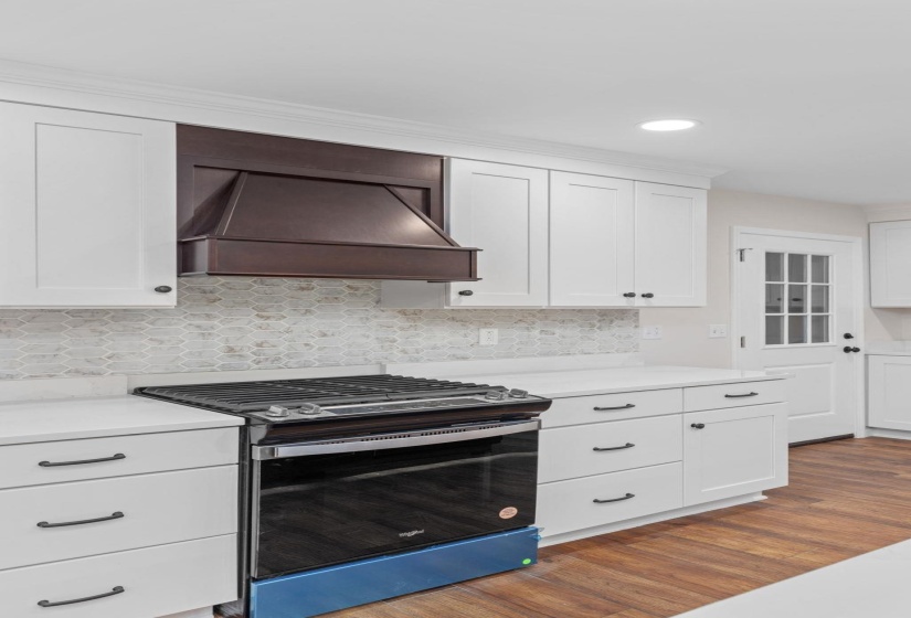 Kitchen with stainless steel gas range oven, custom range hood, white cabinets, dark wood finished floors, and light countertops