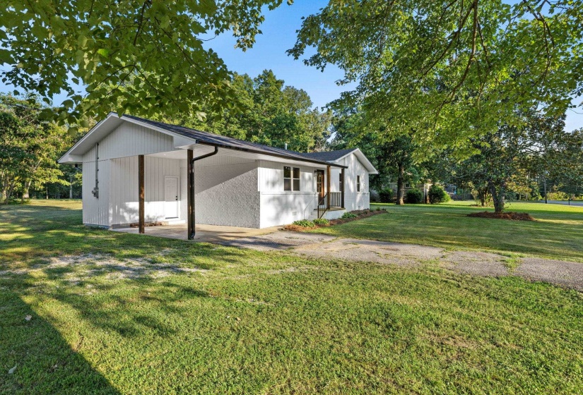 View of side of property with a yard, an attached carport, driveway, and view of wooded area