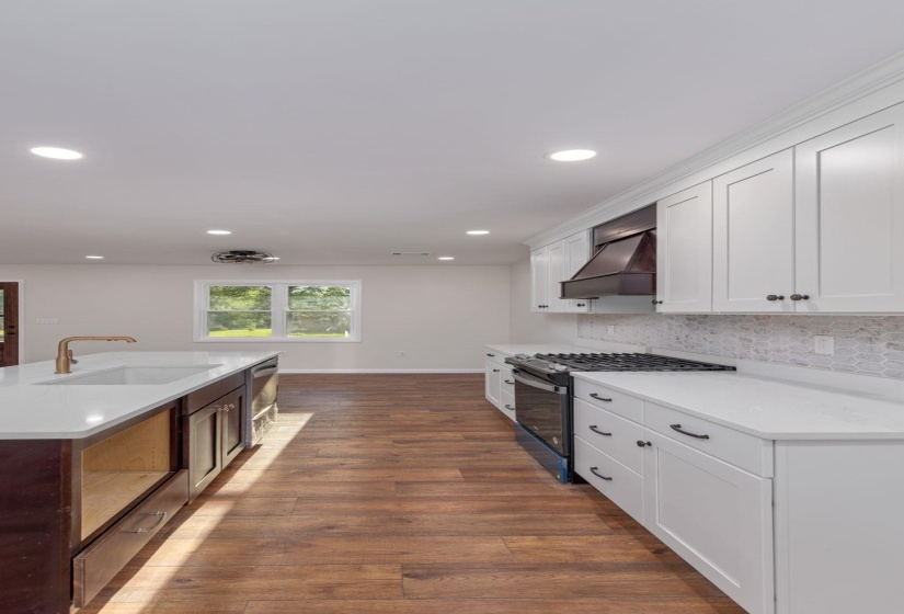 Kitchen featuring gas stove, premium range hood, white cabinets, backsplash, and light countertops