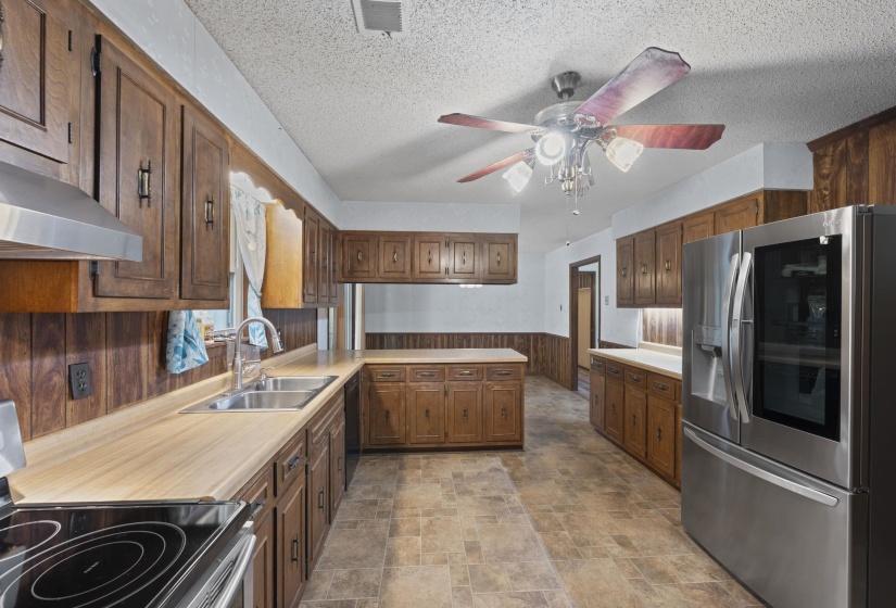 Kitchen featuring extensive wood cabinetry, wood-finish countertops, stainless steel appliances, and a ceiling fan with integrated lighting