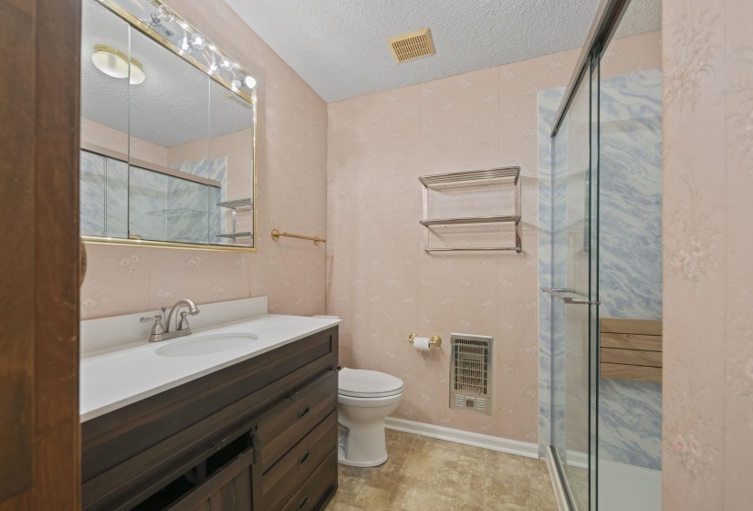 Bathroom featuring a dark wood-finish vanity with a white countertop and integrated sink, a mirrored medicine cabinet with overhead lighting, a glass-enclosed shower with a built-in bench, and light-toned flooring