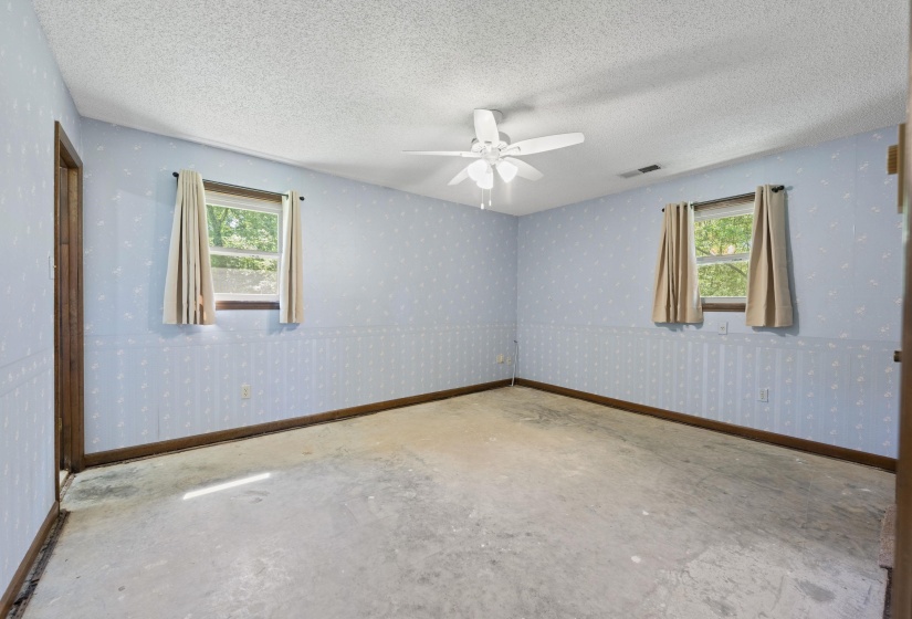Spacious interior room featuring two windows, a ceiling fan, and light blue patterned wallpaper