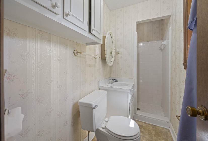 Bathroom featuring a walk-in shower with tile surround, white vanity, built-in upper cabinetry, and patterned wallpaper