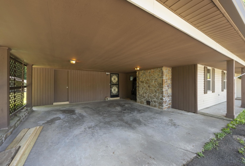 Spacious covered carport featuring a concrete slab, stone column, and direct entry access