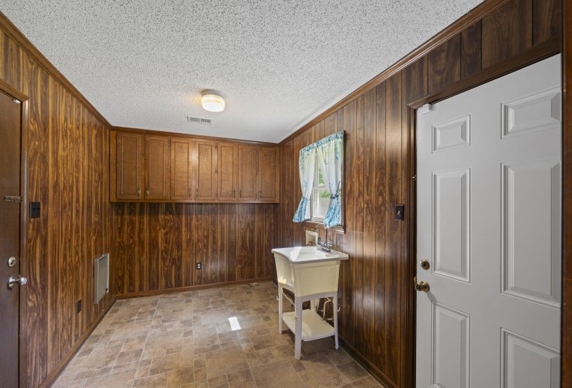 Functional utility room featuring wood-panel walls and a drop-in utility sink
